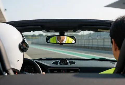 Vue depuis l'intérieur d'une voiture de course, un instructeur en gilet jaune reflété dans le rétroviseur, prêt à prendre la piste.