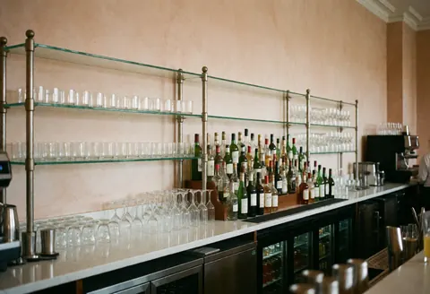 Comptoir de bar festif orné de bouteilles d'alcool et de verres disposés, sur fond de murs en terre cuite, dans un cadre professionnel et soigné.
