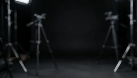 Fond d'étude sombre avec des trépieds et des lumières diffuses, idéal pour ajouter du texte dans un environnement professionnel et calme.