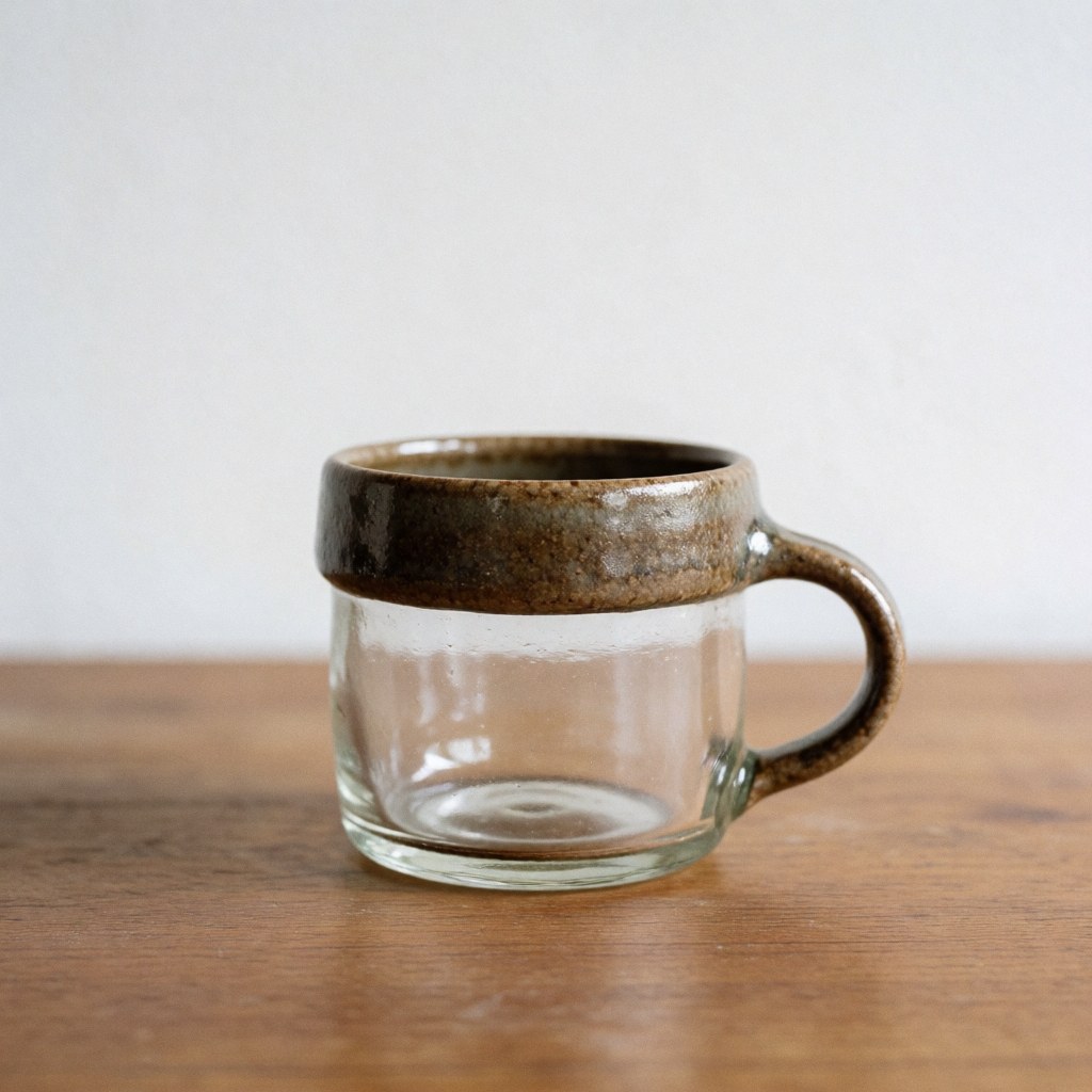 Mug en verre transparent avec bord texturé posé sur une table en bois, fond blanc, lumière naturelle, produit artisanal de verrerie