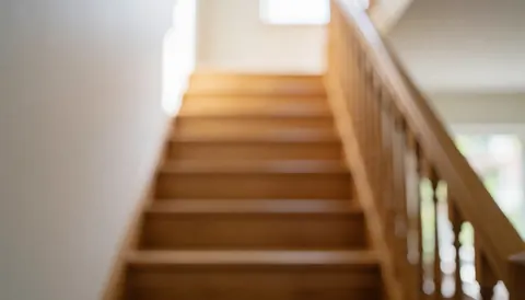 Escalier en bois avec une rambarde visible sur un fond naturel flou, offrant un espace neutre idéal pour l'ajout de textes commerciaux.