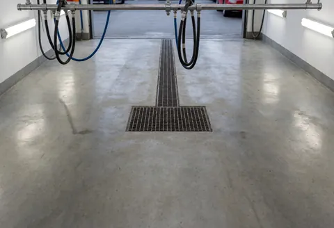 Vue d'un poste de lavage automobile équipé d'une robinetterie en métal sur un sol en béton sous un éclairage fluorescent.
