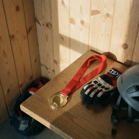 Médaille d'or avec ruban rouge, gants d'escalade et casque posés sur une table en bois avec des murs en panneaux de bois.