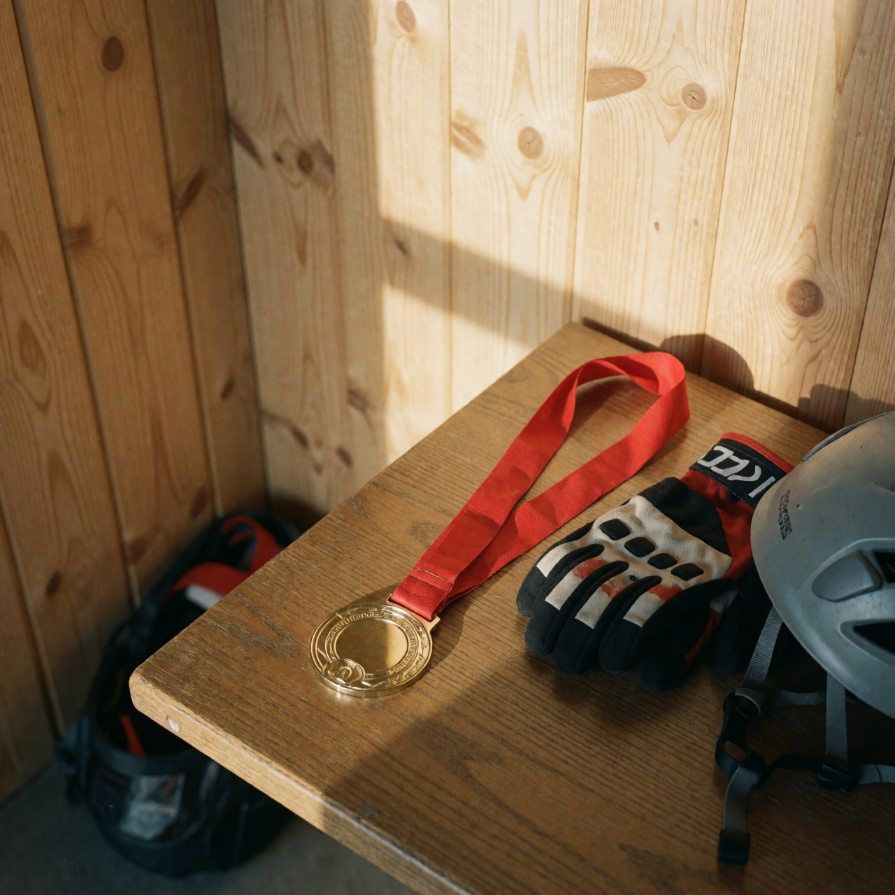 Médaille d'or avec ruban rouge, gants d'escalade et casque posés sur une table en bois avec des murs en panneaux de bois.