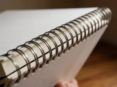 Gros plan détaillé sur la fermeture métallique d'un cahier blanc posé sur une surface en bois aux tons chauds, mettant en valeur la texture du papier et les détails du produit.