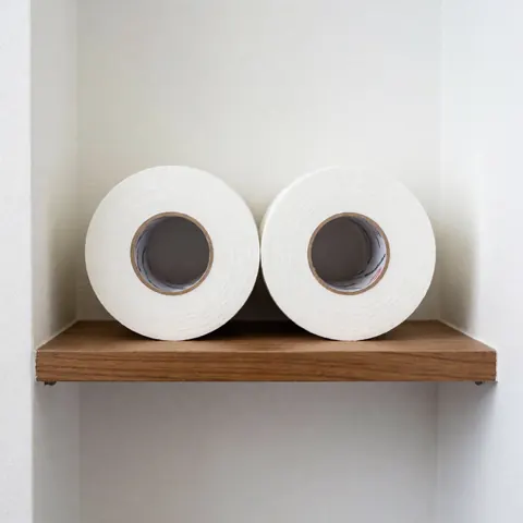 Deux rouleaux de ruban adhésif sportif blanc propre et neuf posés sur une étagère en bois contre un mur blanc, éclairage uniforme.