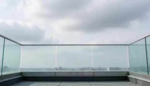Fond de terrasse moderne avec barrière vitrée et ciel couvert, idéal pour services de nettoyage de vitrines. Espace supérieur libre pour texte ou logo.