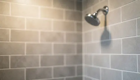 Fond de douche composé de carreaux gris et de joints blancs, avec une paroi en verre chromée dans le coin, éclairage doux et chaleureux, idéal pour mettre en avant des textes ou des services liés à l'installation de