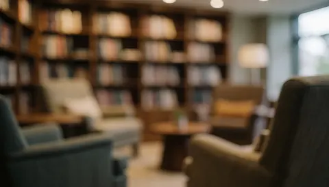 Arrière-plan chaleureux et flou d'une salle de lecture avec des fauteuils confortables et des étagères remplies de livres, offrant un cadre calme pour l'éducation.