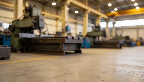 Fond flou d'un atelier industriel avec du matériel métallique, des piliers et un sol en béton, éclairage chaud, idéal pour les textes de services industriels.