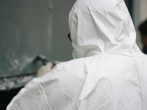 Gros plan sur la fermeture d'épaule d'une combinaison Tyvek blanche avec des gouttes d'eau, montrant la texture et les coutures sur fond industriel flou.