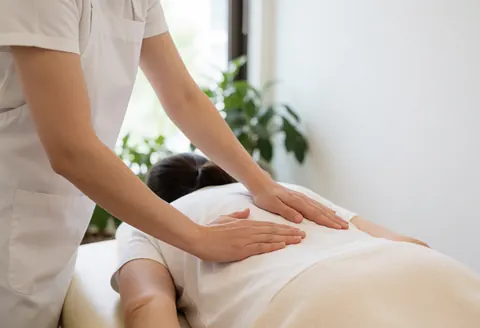 Un thérapeute réalise un massage de tissus profonds en clinique avec lumière naturelle, mains et outils visibles dans un environnement relaxant.
