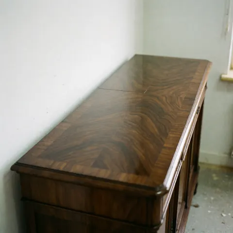 Ancien meuble en bois avec un fini brillant qui reflète la lumière sur des murs blancs et un sol poussiéreux.