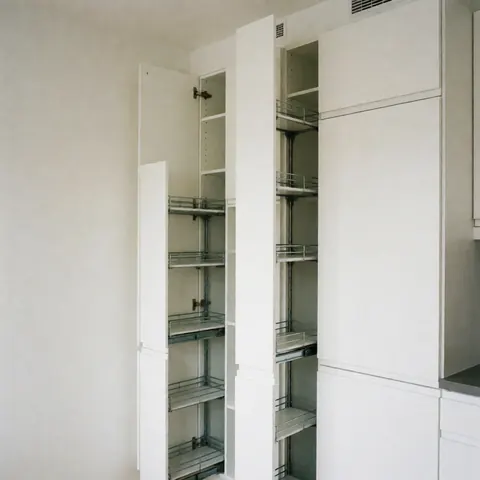 Cuisine compacte dotée d'armoires blanches et d'étagères pliables, aux murs lisses, baignée de lumière naturelle, idéale pour les petits espaces.