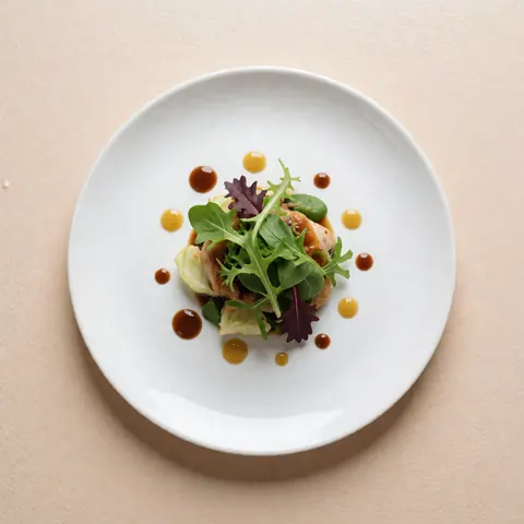 Assiette blanche contenant une salade verte accompagnée d'une sauce marron et jaune sur un fond beige doux.