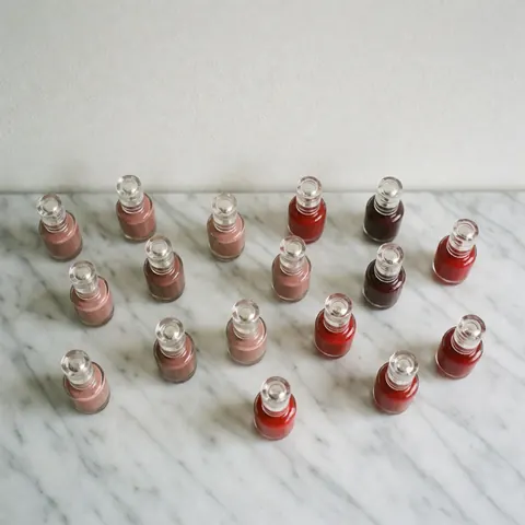 Plusieurs flacons de vernis à ongles aux tons nude et rouge posés sur une surface en marbre blanc, vue de dessus, idéal pour un catalogue de produits de beauté.