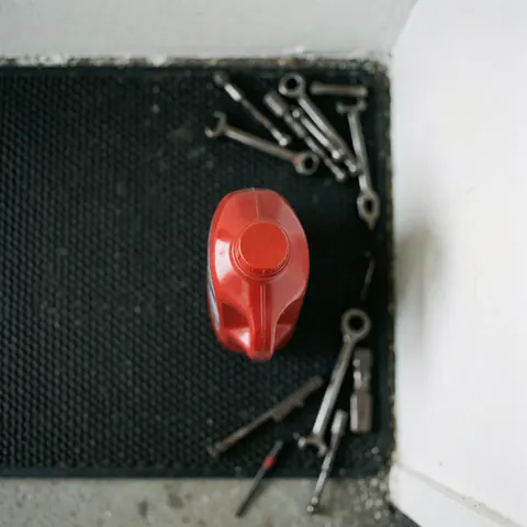 Vue de dessus d'une bouteille rouge contenant du liquide, posée sur un tapis noir avec des clés à rotule dispersées autour dans un atelier mécanique.
