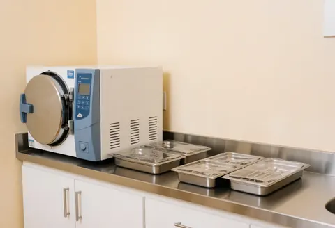 Chambre d'sterilisation médicale équipée de plateaux métalliques scellés posés sur un plan de travail en acier inoxydable dans une salle clinique propre et vide.