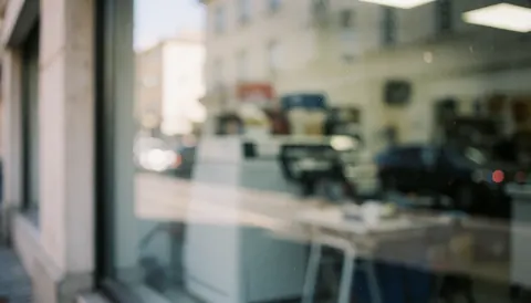Arrière-plan neutre et professionnel d'une devanture de commerce avec une vitrine floue, des reflets de rue et une lumière naturelle douce pour insérer du texte.