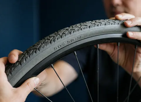Mains d'un mécanicien ajustant la jante d'un vélo, montrant la bande de roulement et les spécifications, contre un mur bleu profond.