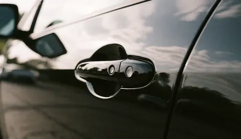 Gros plan d'une porte de voiture noire affichant une finition impeccable et des reflets lumineux du ciel, illustrant la qualité de la carrosserie.