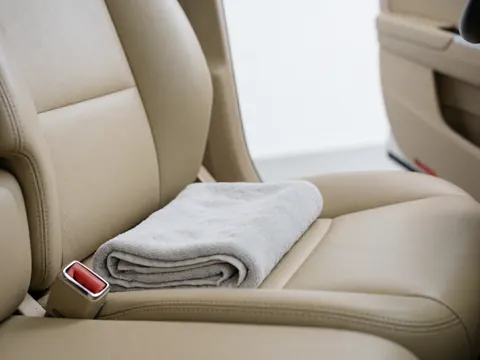 Serviette grise pliée sur un siège en cuir beige. La ceinture de sécurité est visible. L'intérieur du véhicule est net, mettant en avant l'hygiène et le confort.
