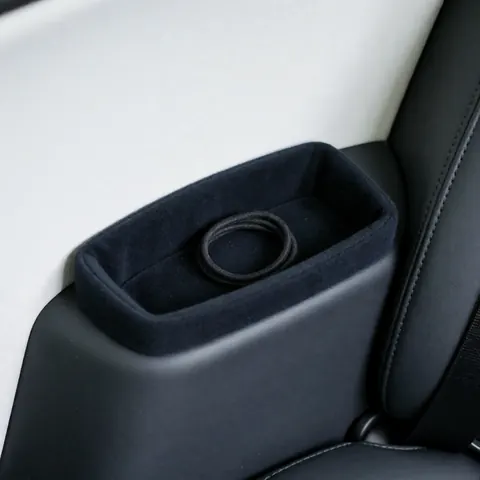 Détail d'un coussin noir posé sur l'assise d'un taxi, accompagné d'un élastique pour les cheveux, le tout sur un fond blanc propre et ordonné.