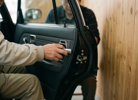 Gros plan sur une main adulte réglant le mécanisme d'une porte de taxi avec un fond en bois naturel, mettant en évidence les détails du travail.