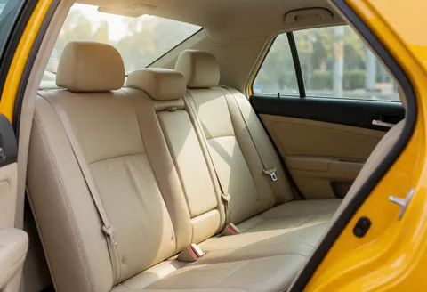 Intérieur d'un taxi jaune avec des sièges arrière beiges propres, ceintures de sécurité visibles et lumière naturelle entrant par les fenêtres.