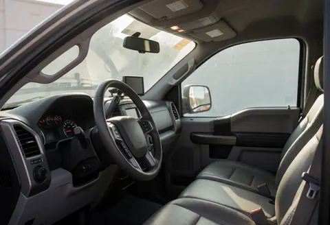 Intérieur propre et bien éclairé d'une camionnette, montrant le volant, le tableau de bord, les sièges en cuir et la lumière du soleil entrant par le pare-brise.
