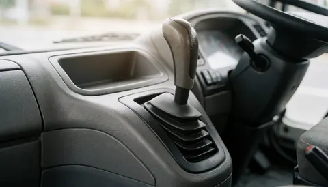 Vue intérieure du levier de vitesses métallique et de la console en plastique texturé d'un camion, baignée d'une lumière douce, offrant un arrière-plan neutre pour insérer du texte commercial.