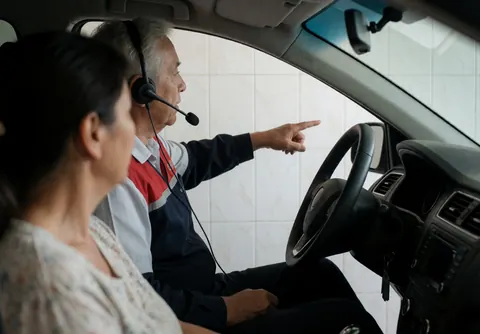Instructeur équipé d'un casque enseignant dans une voiture, murs de carreaux blancs, client écoutant attentivement. Scène réaliste de service de conduite.