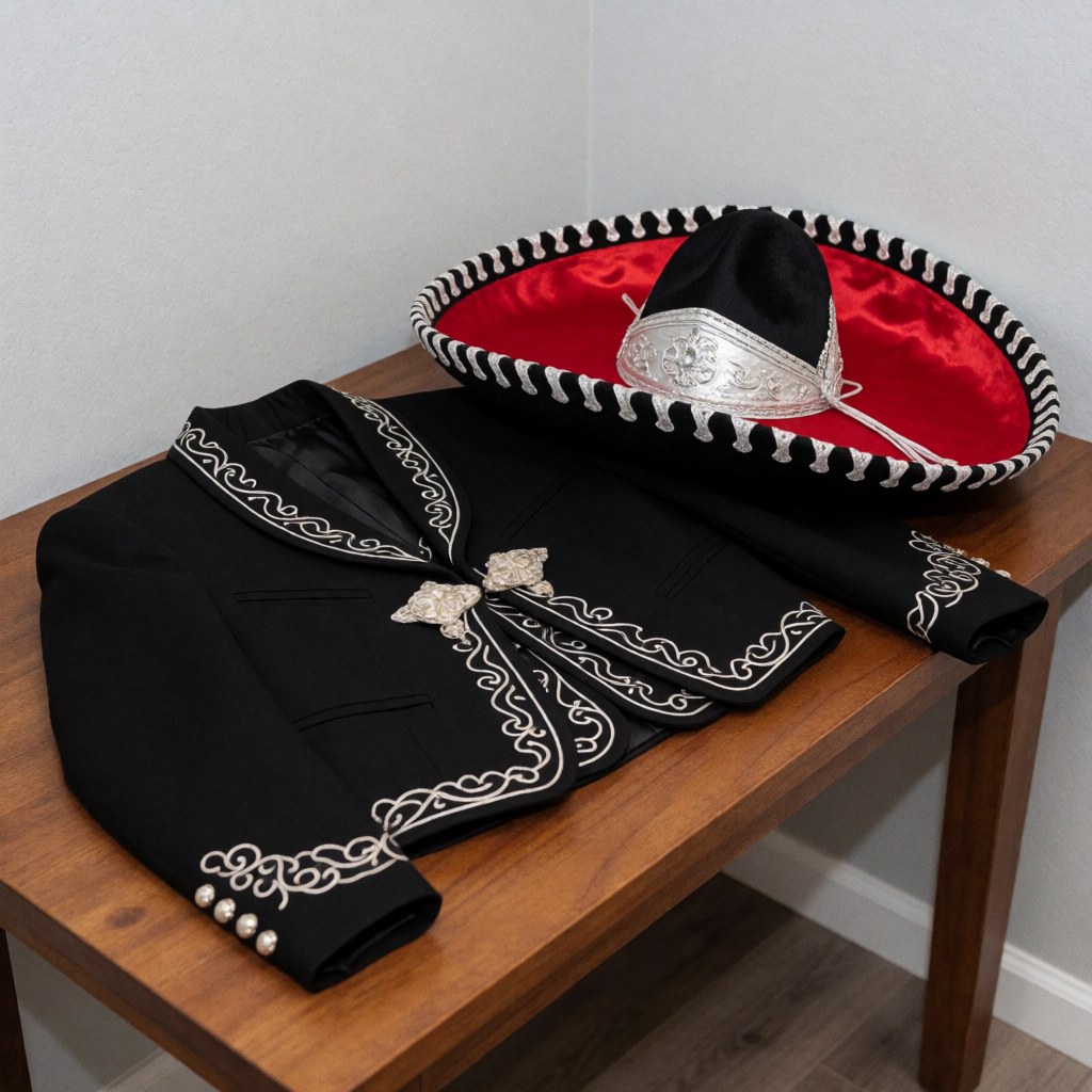 Un costume charro noir orné de broderies argentées et un chapeau à doublure rouge posés sur une table en bois, idéal pour la décoration d'événements.