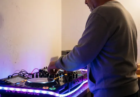 Un dj professionnel utilise un contrôleur pour mixer de la musique sous des lumières néon bleues et violettes, dans une ambiance de fête réaliste.