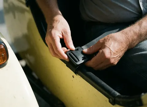 Gros plan des mains d'un adulte ajustant la ceinture de sécurité dans un sidecar jaune. La lumière naturelle met en valeur la texture du tissu et du plastique.