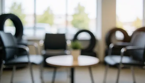 Espace d'attente de garage avec chaises noires, table ronde et pneus en arrière-plan flou, éclairage doux pour texte.