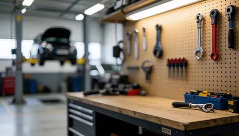 Panneau perforé avec outils suspendus et voiture sur pont élévateur en arrière-plan, servant de fond neutre pour textes commerciaux.
