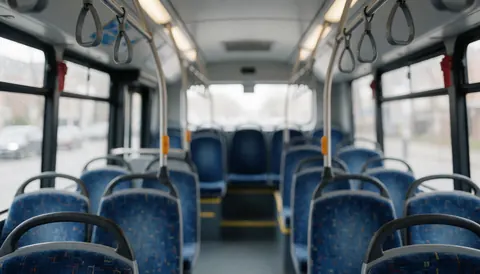Vue intérieure d'un bus public vide montrant des rangées de sièges bleus et des barres métalliques sur un fond flou, adapté comme arrière-plan pour du texte ou du design graphique.