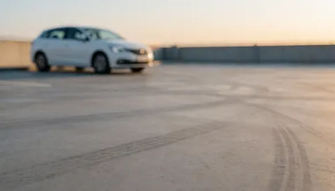 Fond de parking avec traces de pneus, voiture blanche floue, lumière chaude au coucher du soleil, idéal pour textes de services automobiles.