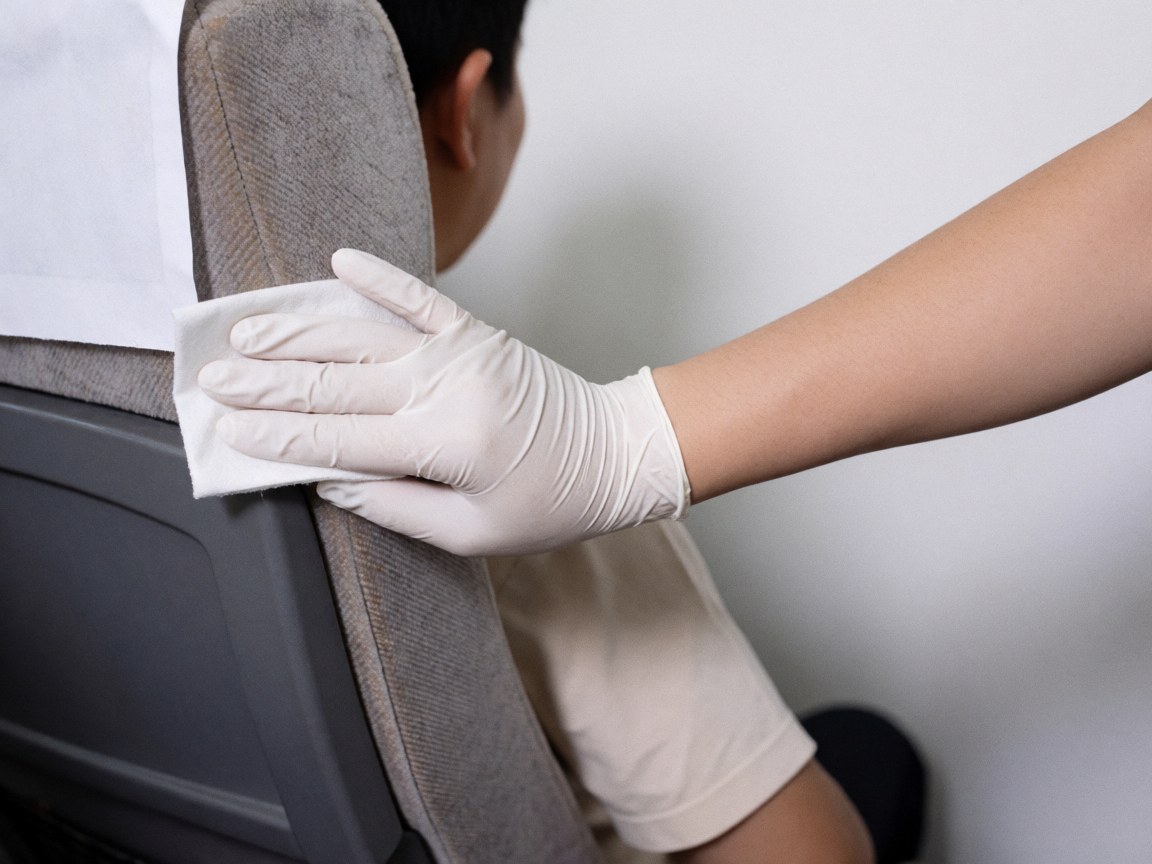 Une main portant un gant blanc utilise un chiffon désinfectant pour nettoyer le tissu d'un siège de bus, illustrant l'hygiène dans les transports.