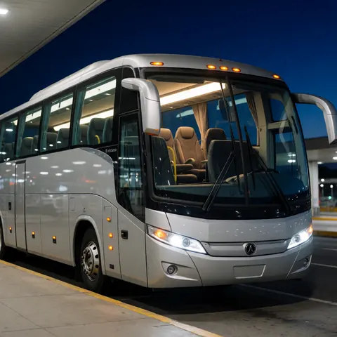 Autobus de tourisme blanc stationné la nuit avec les lumières intérieures allumées et des reflets sur les vitres, évoquant un environnement sûr et professionnel.