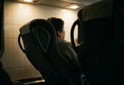 Un passager est installé sur un siège inclinable à l'intérieur d'un autobus de tourisme, profitant d'un voyage nocturne dans un environnement confortable.