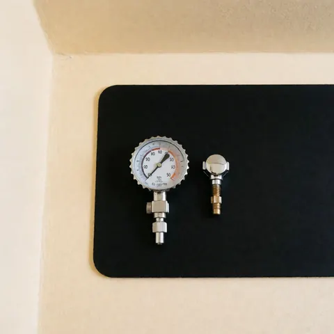 Un manomètre de pression de pneus et un bouchon de valve posés sur une surface noire avec un fond beige, idéal pour l'entretien automobile.