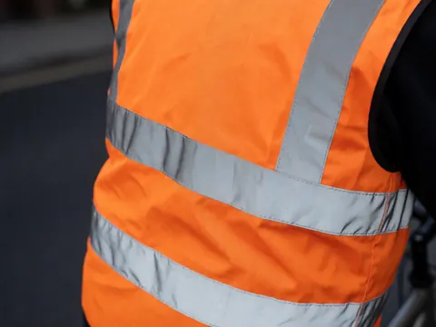 Gilet de sécurité orange avec rayures argentées, idéal pour les taxis vélos. Texture du tissu propre et détails des coutures visibles en gros plan.
