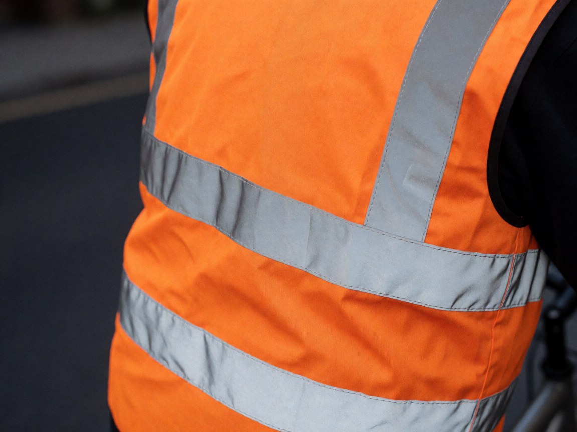 Gilet de sécurité orange avec rayures argentées, idéal pour les taxis vélos. Texture du tissu propre et détails des coutures visibles en gros plan.