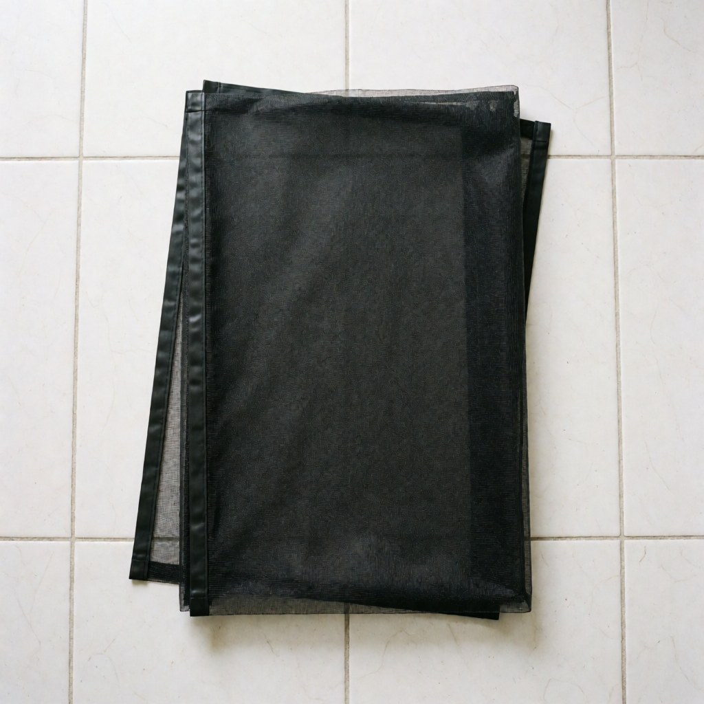 Moustiquaire à fermeture magnétique noire, pliée sur un sol carrelé blanc, prête pour l'installation dans un intérieur.
