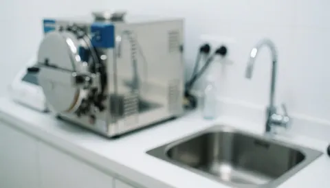 Arrière-plan stérile avec un autoclave métallique et un évier, idéal pour les tatouages. Surface propre, éclairage froid, ambiance professionnelle sans personnes.