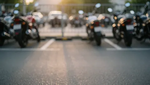 Arrière-plan flou d'un stationnement pour motocyclettes avec la lumière chaude du crépuscule, idéal pour superposer des textes. Asphalte, lignes blanches et silhouettes de motos.