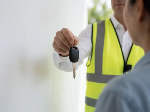 Un agent de parking en gilet jaune remet les clés d'une voiture à un client dans un stationnement professionnel éclairé par la lumière naturelle.