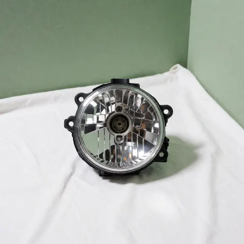 Un phare de voiture neuf et propre posé sur un tissu blanc avec un mur vert pâle en arrière-plan pour illustrer le recyclage automobile.